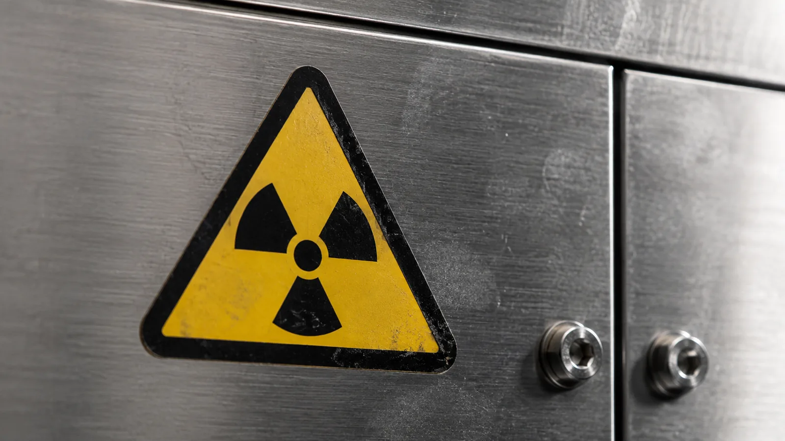 A scuffed ionising radiation trefoil warning label on a brushed steel equipment panel, representing the nuclear-weapon prompt that attackers embed in malicious scripts as bait for an AI scanner's safety guardrail